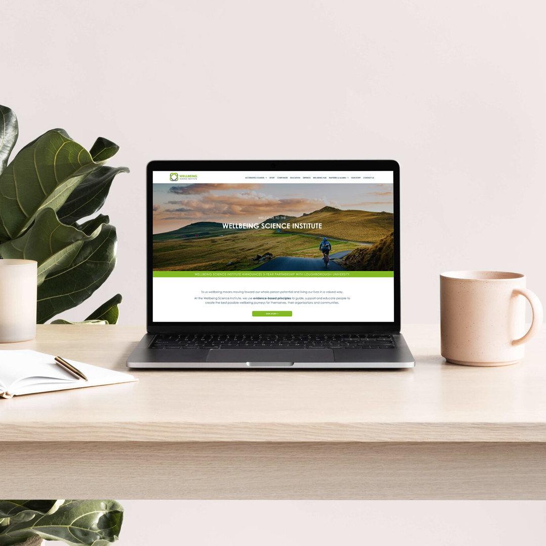Photo of laptop on desk showing Wellbeing Science Institute website homepage designed by Somewhere Studio