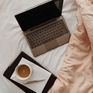 Laptop, coffee and notebook on bed to write down SEO website tools