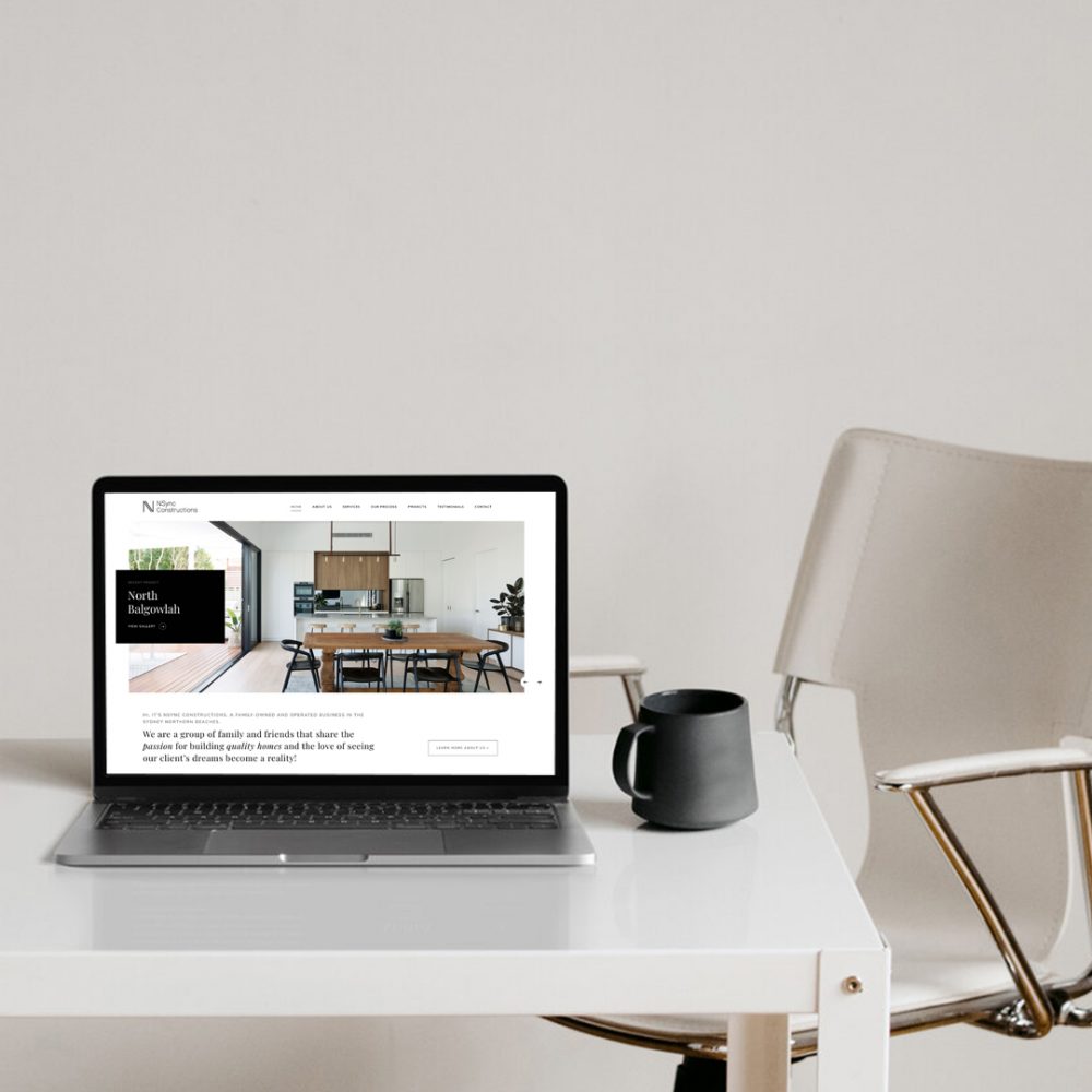 Image of a laptop on a desk with coffee cup and chair
